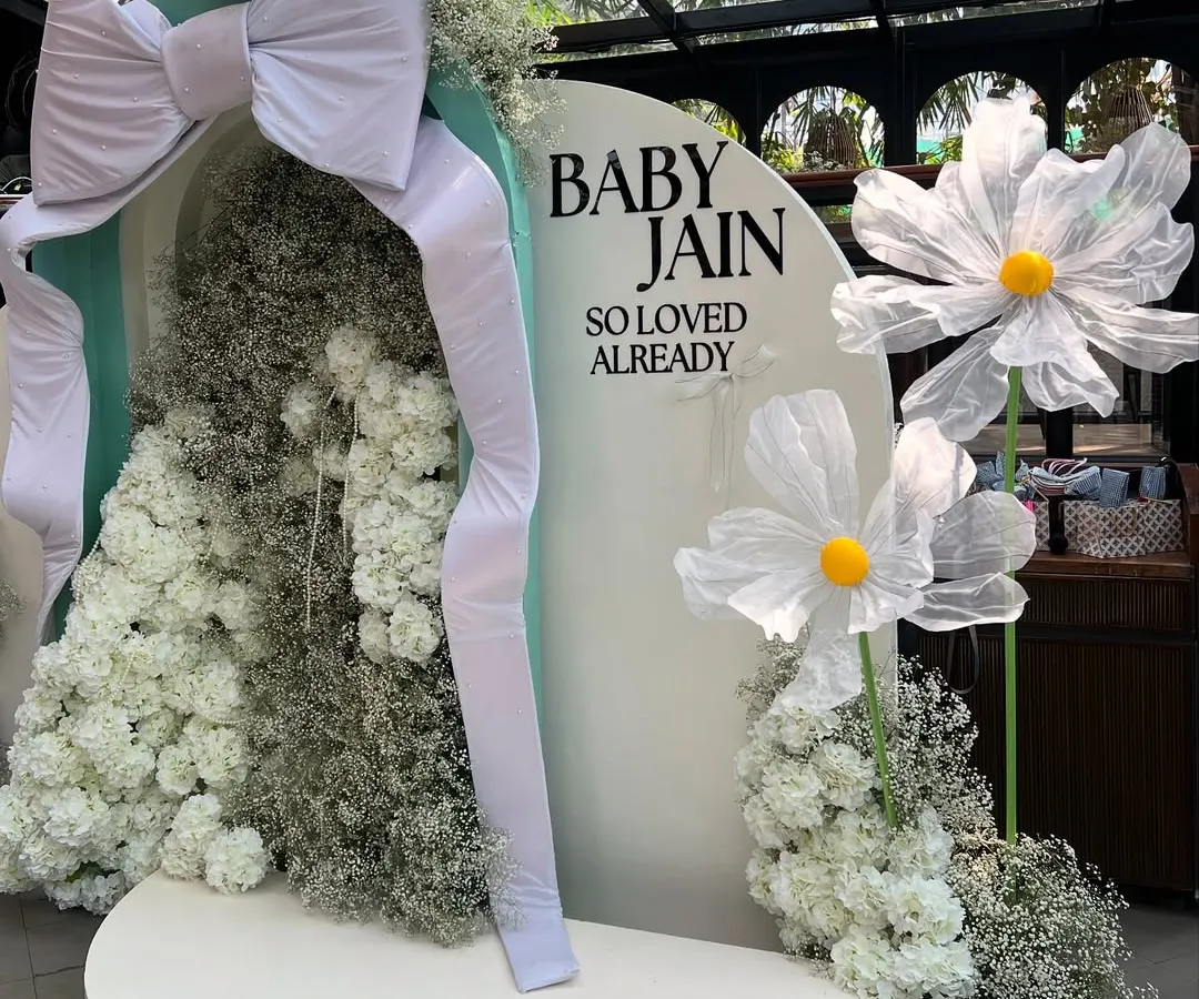 For this dreamy baby shower, we created a bespoke backdrop featuring a giant fabric bow, clouds of baby's breath, and oversized whimsical daisies. This is our signature modern and chic event styling.