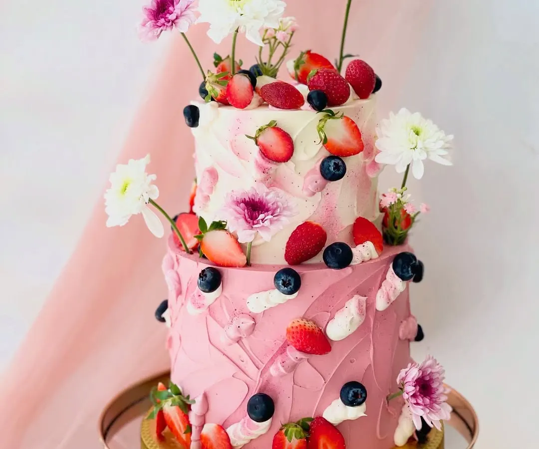 This vibrant two-tiered cake showcases a playful yet elegant design with textured pink buttercream, fresh strawberries, blueberries, and white chrysanthemums. It's a perfect example of how I combine fresh flavours and artistic decoration.