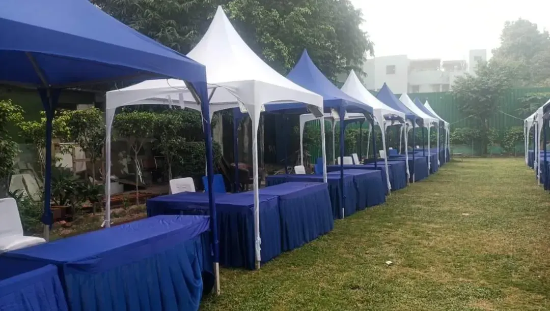 For exhibitions and trade shows, I can set up clean and professional stalls using pagoda tents or canopies. This setup in Greater Noida features a long row of stalls, each with its own table, ready for vendors.