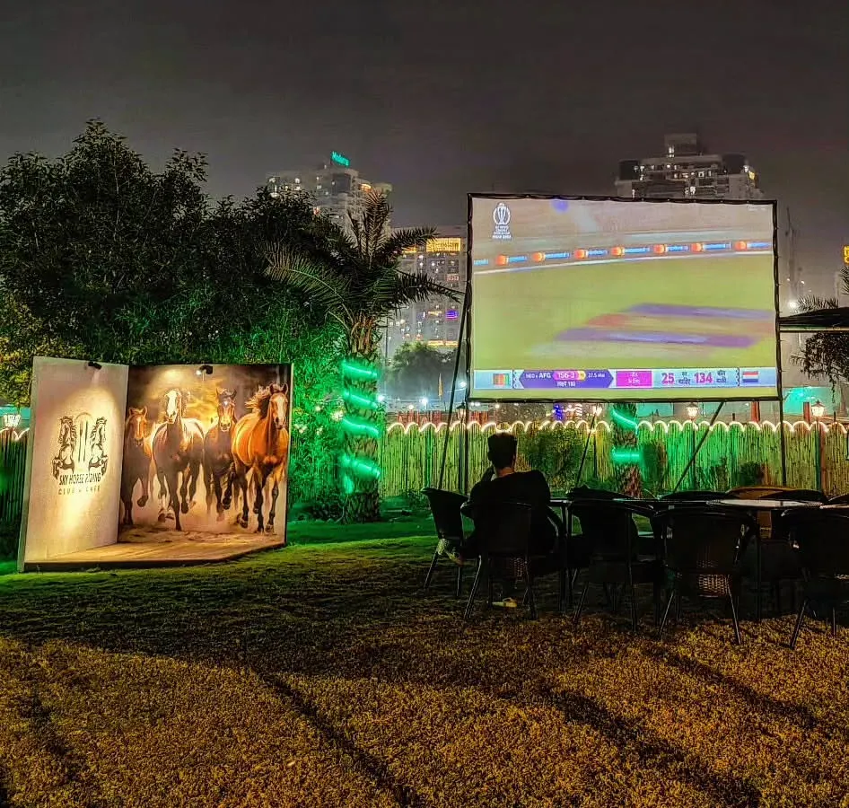 We host outdoor sports screenings on a giant projector, creating a mini-stadium feel. Here, guests enjoy a live cricket match on our lawn, a perfect setup for a community sports night.