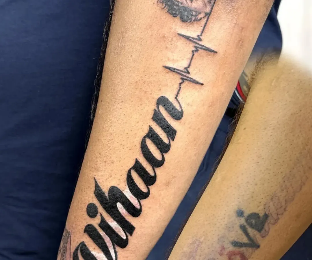 We turned a faded memory into a timeless tribute. This piece was designed to cover an old, colorful tattoo with the name of the client's son, "Vihaan," connected by a heartbeat line to his portrait. It's a beautiful example of how a cover-up can become the most meaningful tattoo of all.