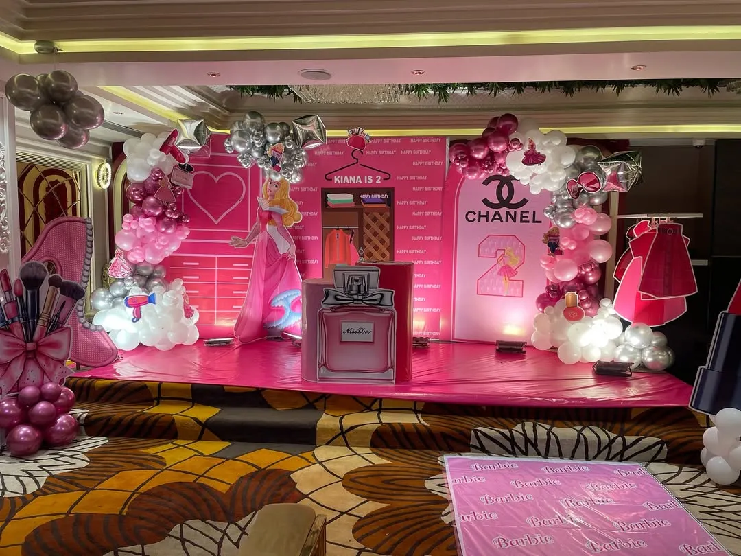 We brought a little girl's fashion-themed dream to life with this vibrant pink stage for her second birthday. The backdrop includes custom elements like a Chanel logo, a princess cutout, and perfume bottle props, making it a perfect photo opportunity.