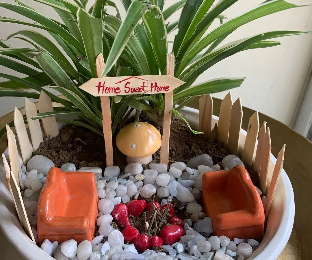 I created this miniature 'Home Sweet Home' garden to be a tiny escape on a desk. It features a spider plant, a quaint picket fence, and a whimsical campfire scene, all designed to bring a smile and a moment of peace to a busy workday.