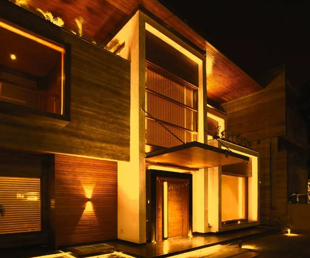This is the entrance to the 'Kohinoor' residence, a project where light was used to enhance the natural warmth of the stone and wood. The design employs a combination of recessed linear lighting, subtle uplights, and focused downlights to create an inviting and luxurious welcome.