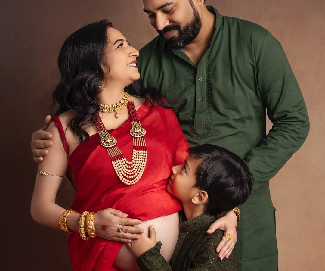 A moment of quiet connection before the family grows. I love how the traditional red saree and jewelry add such elegance to this maternity portrait, while her son's gentle kiss on the baby bump tells a story of love and anticipation.