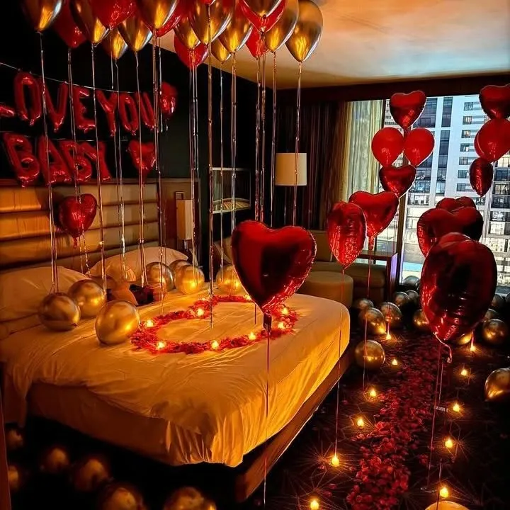 For a truly romantic gesture, we can transform any room into a luxurious retreat. This surprise setup includes a candle-lit rose petal pathway, heart-shaped balloons, and "I Love You Baby" foil letters sentimientos on the bed.