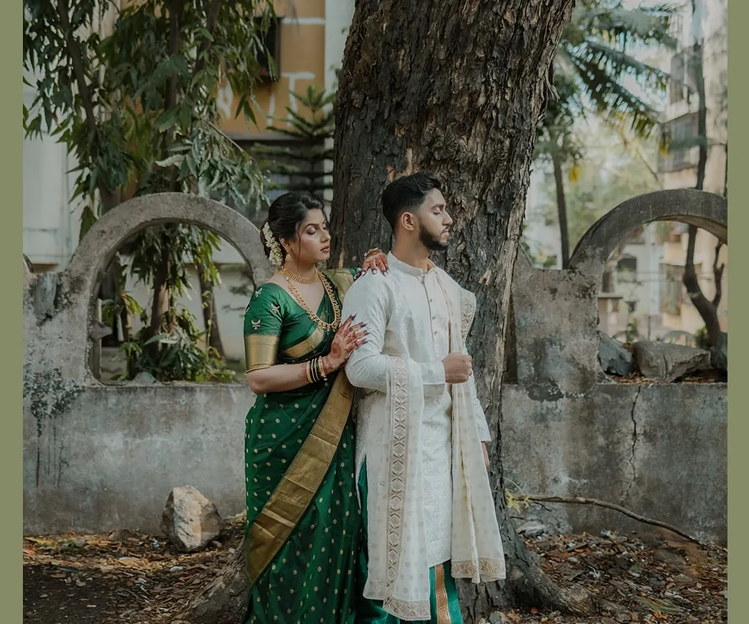 Showcasing classic Marathi elegance, this couple's portrait is set against a rustic tree and stone wall. Her deep green Nauvari saree and his white kurta create a timeless look, perfect for heritage-themed engagement photos.