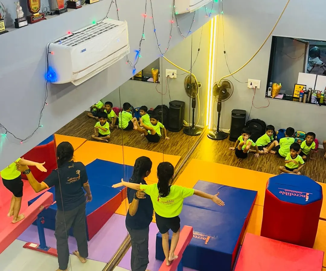 A bird's eye view of a typical gymnastics class at our Gorai studio. You can see children practicing on low balance beams with instructor assistance, while others wait their turn, showcasing our structured and supervised class environment.