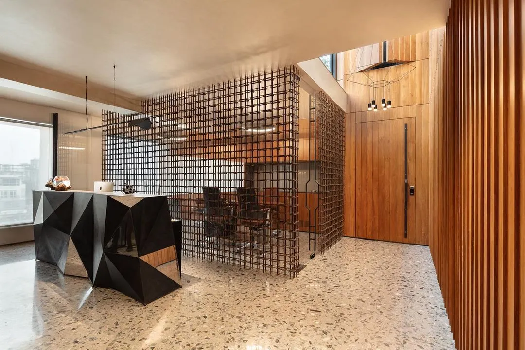 For a construction firm's office in South Delhi, we contrasted raw and refined materials. The reception features a faceted steel desk, terrazzo flooring, and a visually permeable screen made from repurposed rebar, creating a compelling composition that speaks to the client's industry.
