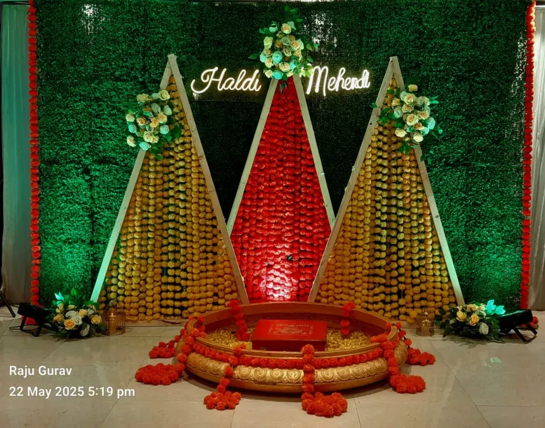 This is a vibrant Haldi and Mehendi stage I created. It uses a traditional green grass wall backdrop with geometric structures made of marigold flowers and a custom neon sign, perfect for pre-wedding ceremonies.