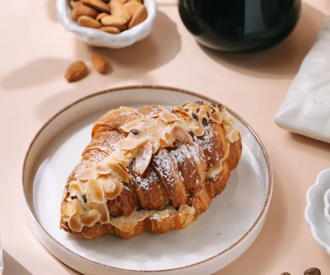 A bright and inviting shot of an almond croissant and coffee, perfect for a bakery's menu or social media. I styled this to create a perfect morning mood, highlighting the flaky pastry and fresh ingredients to attract customers.