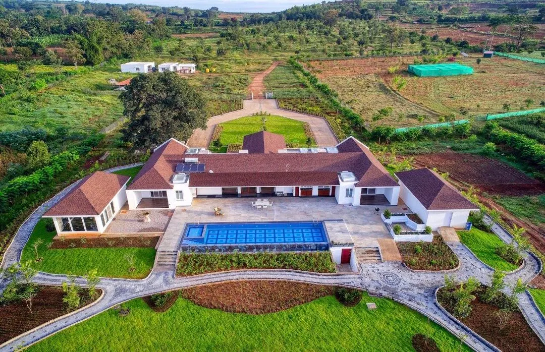 An aerial view of a sprawling farmhouse we designed by the backwaters of Kabini. The architecture is planned for symmetrical elegance, integrating the residence, infinity pool, and extensive landscaping into a cohesive, luxurious estate.
