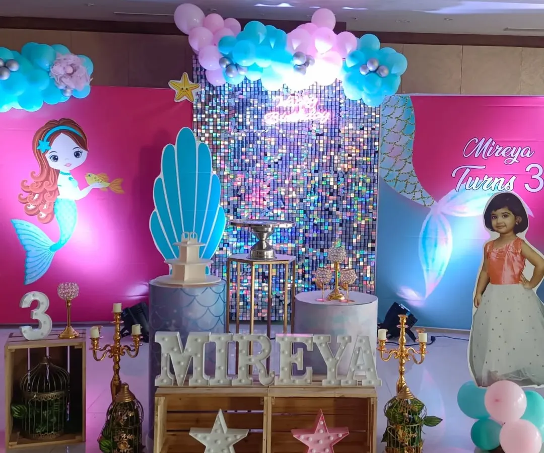 For this third birthday, I created a full mermaid theme. The setup includes a silver shimmer wall for sparkle, character cutouts, a personalized life-size cutout of the birthday girl, and themed pedestals for the cake and desserts.