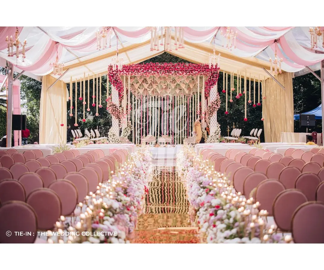 Inspired by the bride's Kanchivaram saree, this Muhurtham ceremony is a testament to our personalized design approach. The aisle is lined with a garden of roses leading to a magnificent floral mandap, all under a canopy of pink and white draped fabric, creating an atmosphere of regal elegance.
