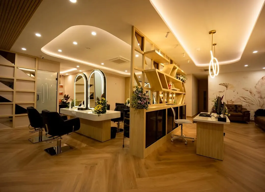 This wide-angle view captures the salon's main floor, showcasing the seamless flow between the reception and styling areas. We designed the custom geometric shelving unit as a functional art piece, complemented by soft, layered ceiling lights to create a warm and sophisticated ambiance.