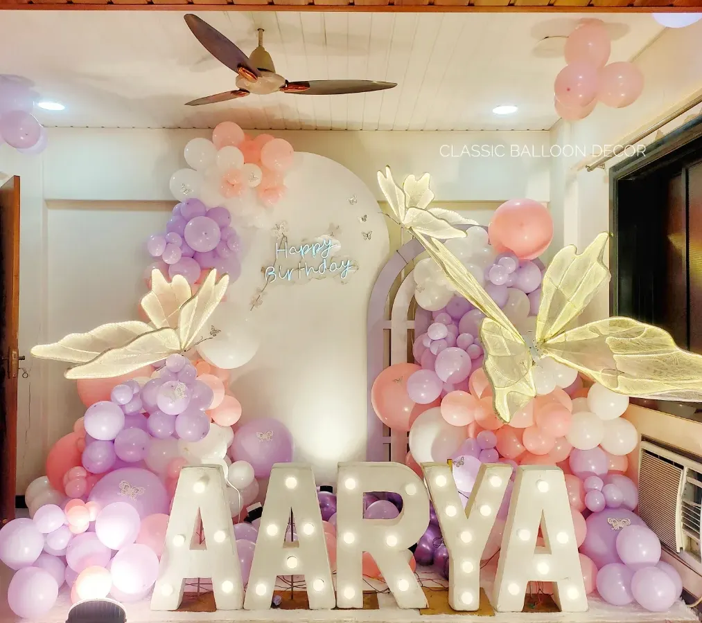 For baby Aarya's first birthday, we created this magical butterfly-themed photo corner. The setup features large marquee letters for the name, soft pastel balloon garlands, and beautiful illuminated butterfly wings.