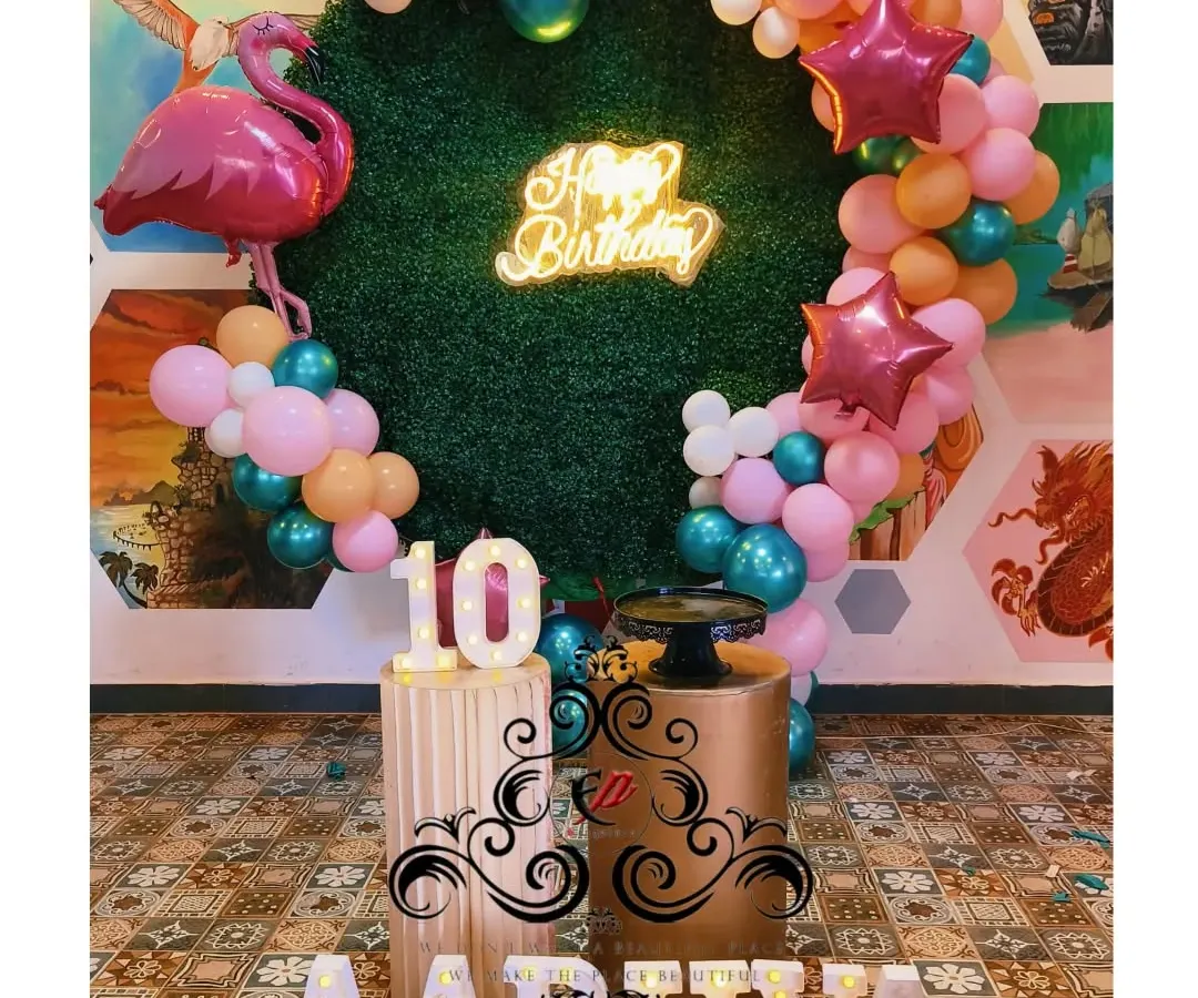 For birthdays, I bring any theme to life. This tropical jungle theme for a 10th birthday includes a custom grass backdrop, a neon 'Happy Birthday' sign, themed balloon arrangements, and light-up marquee numbers.