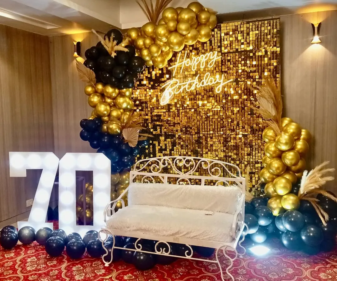 For a glamorous 70th birthday, we designed this stunning photo booth with a gold shimmer wall, a custom 'Happy Birthday' neon sign, and bold marquee numbers. The black and gold balloon arrangement adds a touch of sophisticated fun.