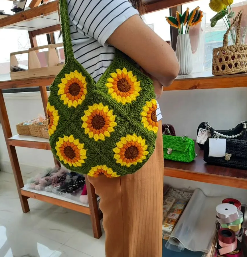 Here is my handmade crochet tote bag with a vibrant sunflower granny square pattern. I used a deep green yarn for the base to make the yellow and brown sunflowers stand out. The bag is shown here being worn to give you an idea of its size and how it hangs from the shoulder.