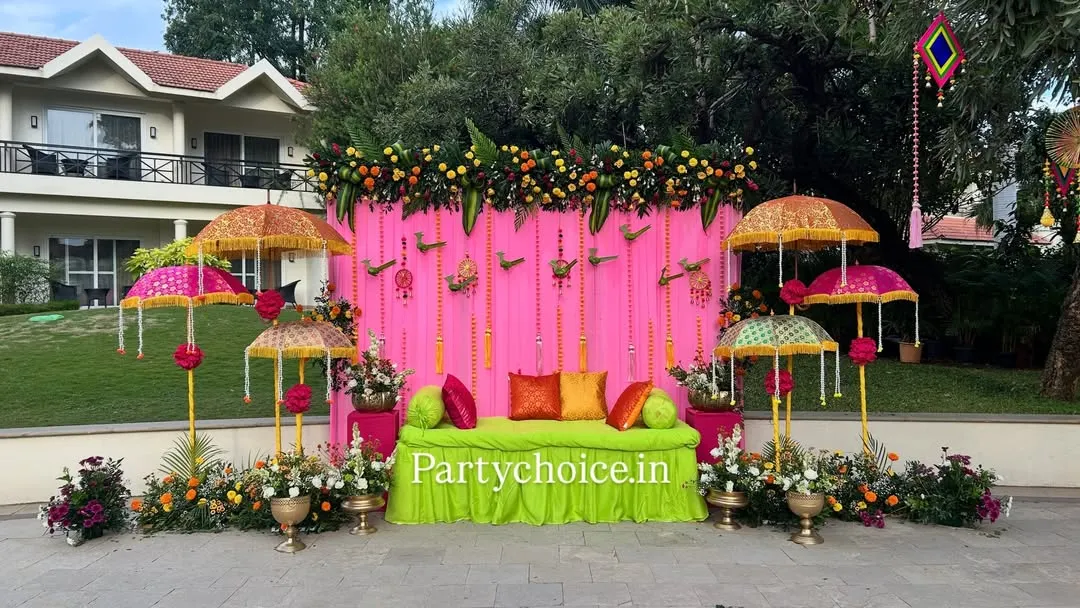 For this outdoor Haldi ceremony, we created a vibrant and festive atmosphere. The setup features a bright pink backdrop, a comfortable lime-green seating area, and decorative Rajasthani umbrellas, all framed by a thick garland of marigolds.