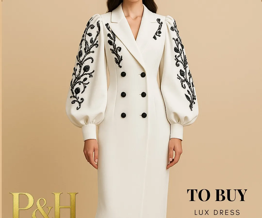 A vision of modern regality, this image showcases a model in a pristine white, double-breasted dress. The design is distinguished by its dramatic puff sleeves adorned with intricate black floral embroidery, creating a powerful silhouette that is both elegant and commanding.