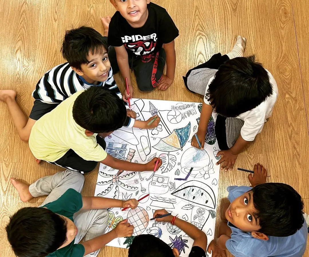 Collaboration in our creative corner. A group of boys works together on a giant coloring sheet, a simple activity that encourages sharing, communication, and collective artistic expression.