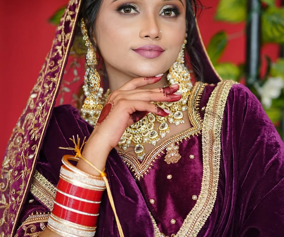 For this stunning North Indian bride, we created a glamorous look with bold, smoky eyes and a matte pink lip to complement her rich purple velvet lehenga. The heavy Kundan jewelry, chooda, and maang tikka complete this regal bridal ensemble.