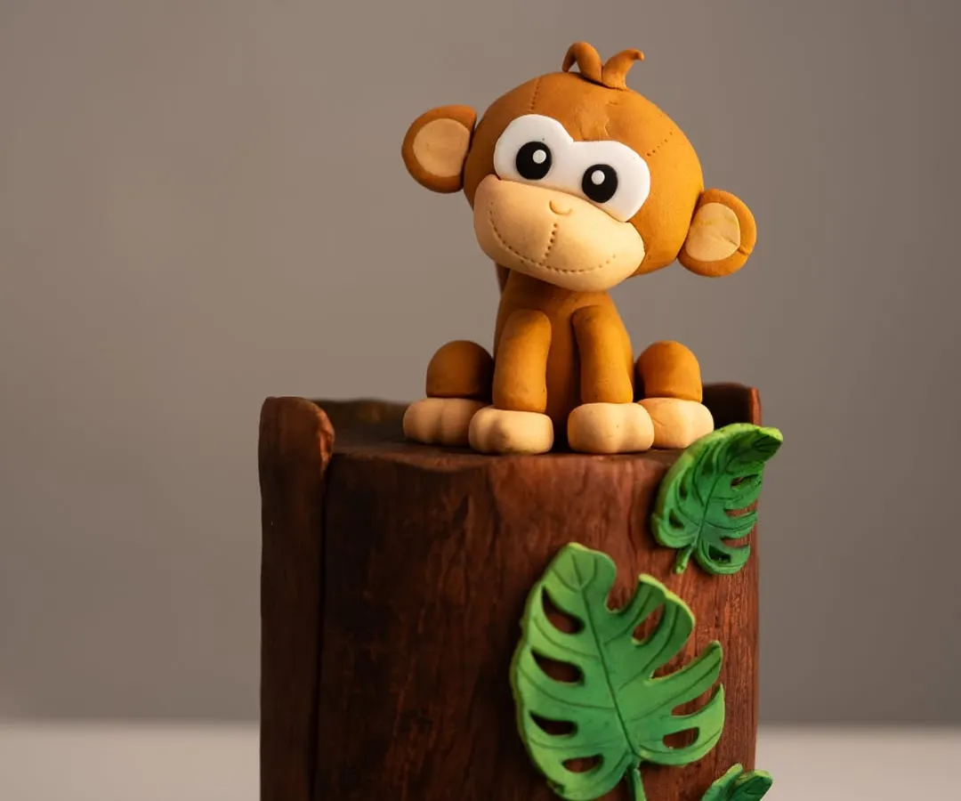 A close-up of a custom fondant cake topper, this adorable monkey sits atop a cake designed to look like a tree stump. This shows the detailed, playful character work I can do for children's birthday cakes and jungle-themed parties.