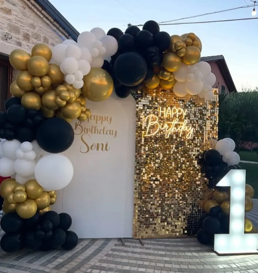 A chic and modern first birthday setup featuring a black, white, and gold color scheme. The gold shimmer wall, custom neon sign, and light-up number '1' create a glamorous photo backdrop for a stylish celebration.