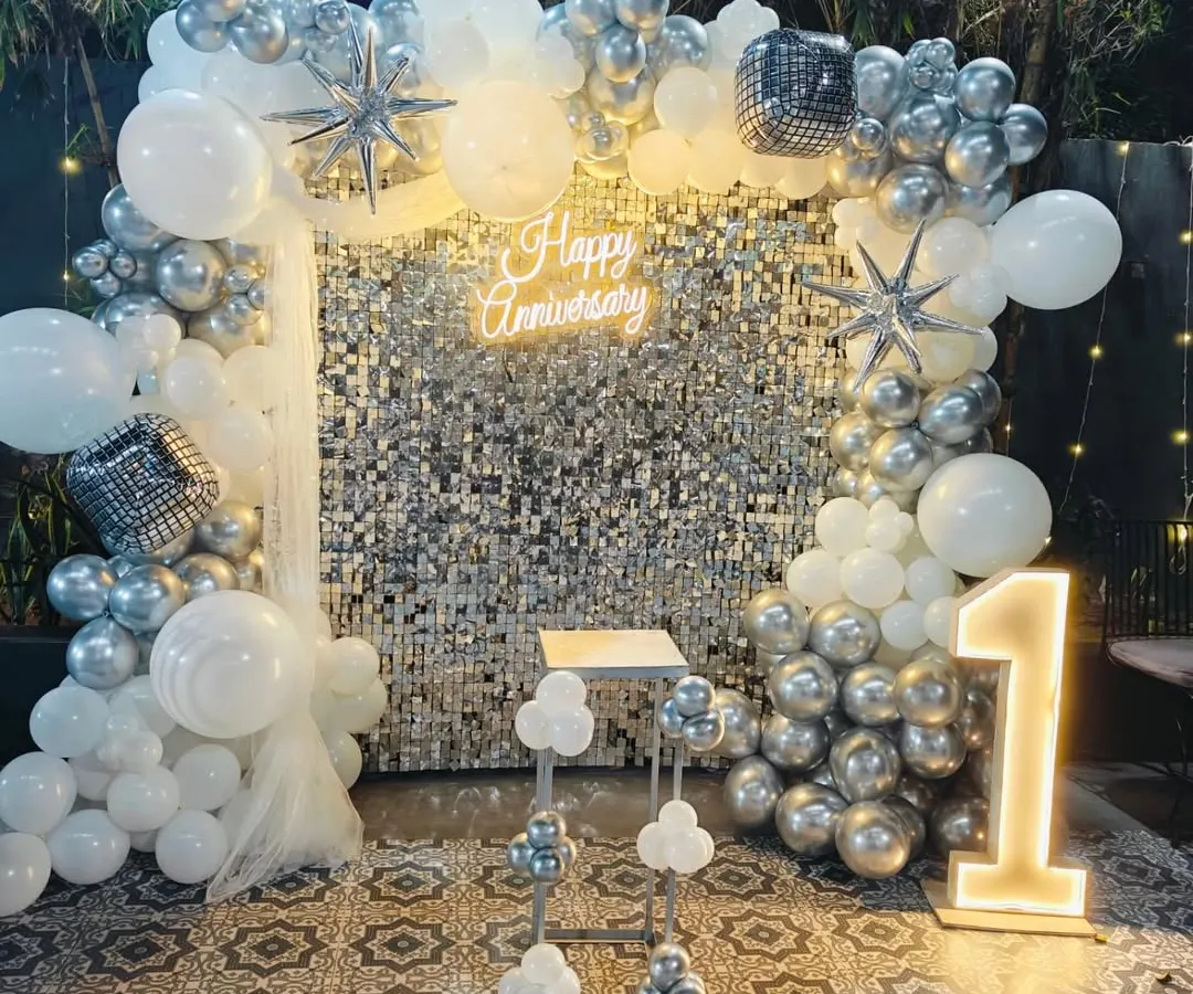 For a chic and modern anniversary party, I designed this stunning photo backdrop. It features a shimmering silver sequin wall, a lush organic balloon arch in silver and white, and a custom neon "Happy Anniversary" sign, all brought together with a light-up number "1" to mark the special milestone.
