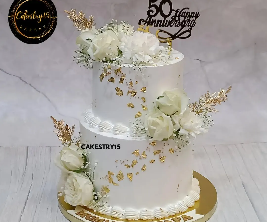 We created this elegant two-tier pineapple cake to honor a beautiful fifty-year love story. It features pristine white frosting, delicate gold leaf accents, and arrangements of fresh white roses, all coming together for a timeless 50th-anniversary centerpiece.