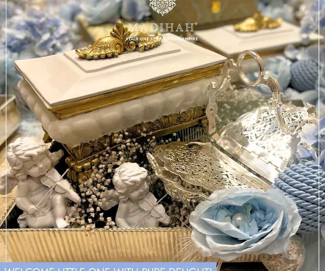 Welcome a little one with this exquisite hamper featuring cherubic angel figurines and soft blue floral arrangements. The design combines classic white and gold accents with silver-plated serveware, making it a perfect luxury gift for a baby boy's arrival.