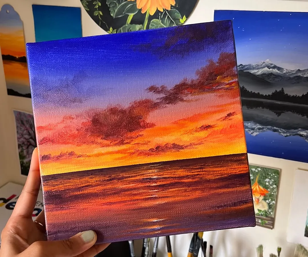A vibrant sunset painting capturing the deep blues of the sky meeting the fiery oranges and purples of the horizon over the ocean. This acrylic on canvas piece is all about the dramatic and beautiful colors of a beach sunset.