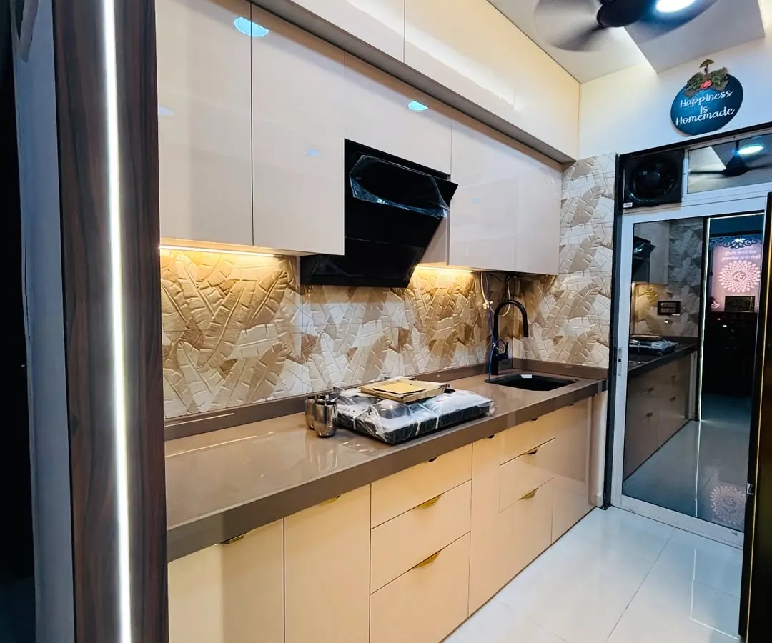 This parallel kitchen design creates a warm and luxurious feel with high-gloss beige cabinets and ambient lighting. Note the textured stone backsplash and integrated black chimney, creating a seamless and elegant workspace.