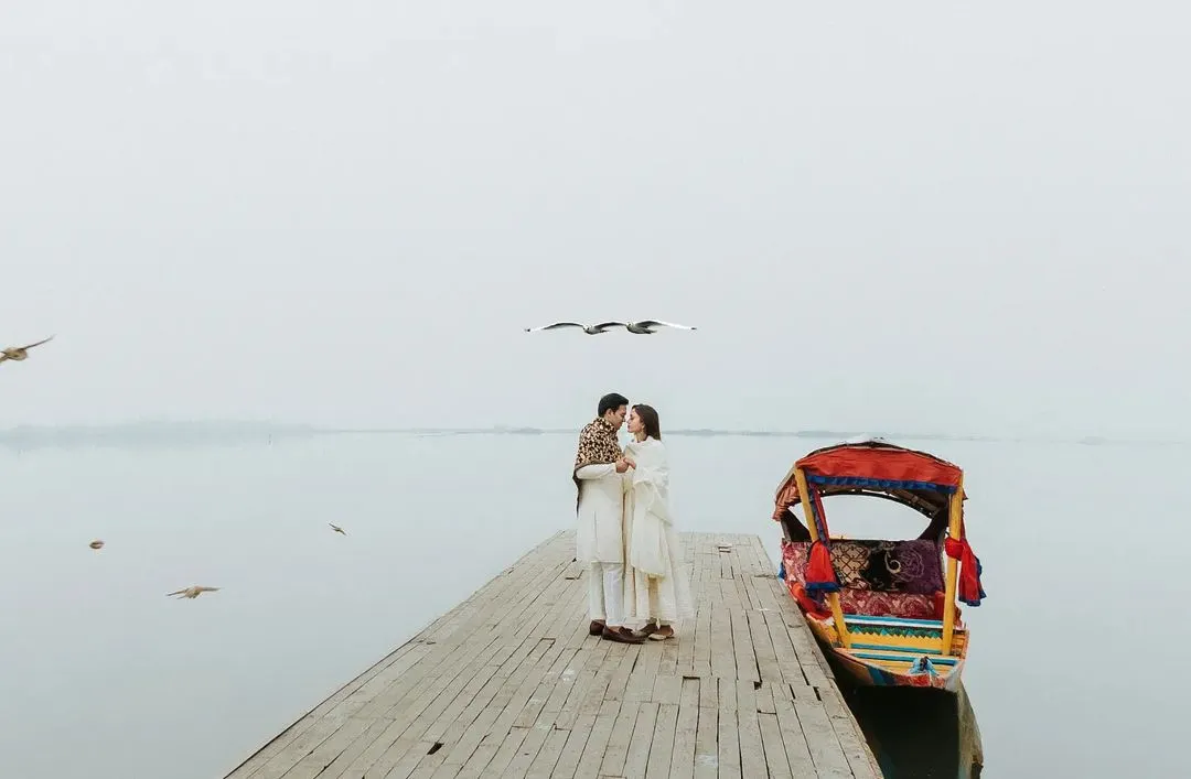An intimate moment on a quiet dock in Kashmir, with birds flying overhead against a misty, minimalist landscape. This image captures the serene, fairytale-like atmosphere of our destination pre-wedding shoots.