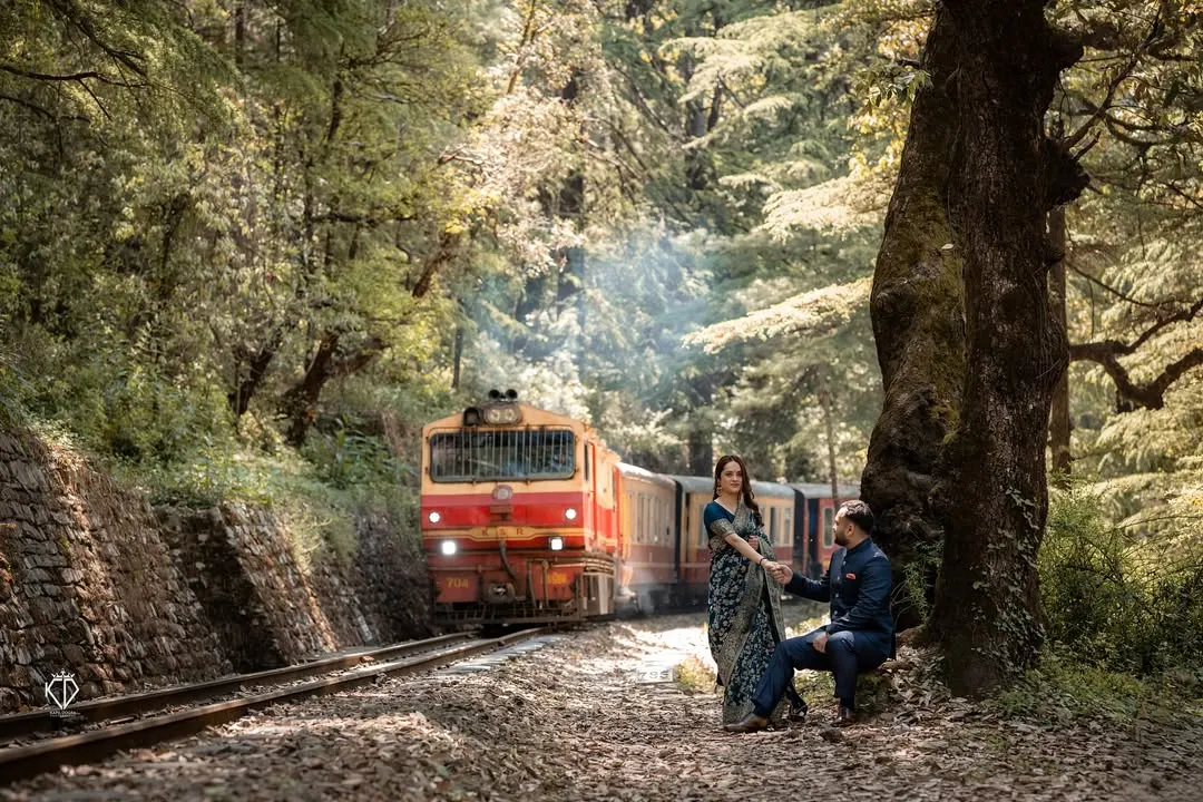 The iconic Shimla toy train passes by as the couple shares a quiet moment, blending history and romance. This shot captures the timeless charm of a classic Himalayan pre-wedding photoshoot.
