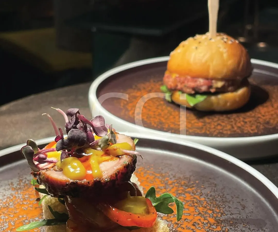 We believe luxury is in the details. This showcases two of our popular gourmet appetizers: a perfectly crafted mini burger and an open-faced canapé with delicate toppings, demonstrating our flair for modern, bite-sized culinary creations.