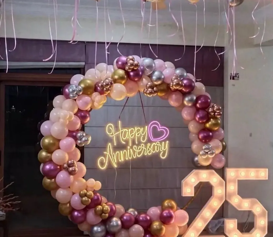 For this 25th anniversary party at home, we created a beautiful focal point with a full balloon ring in shades of pink, rose gold, and silver. The "Happy Anniversary" neon sign and large light-up marquee numbers for the milestone year made the space feel special and festive.