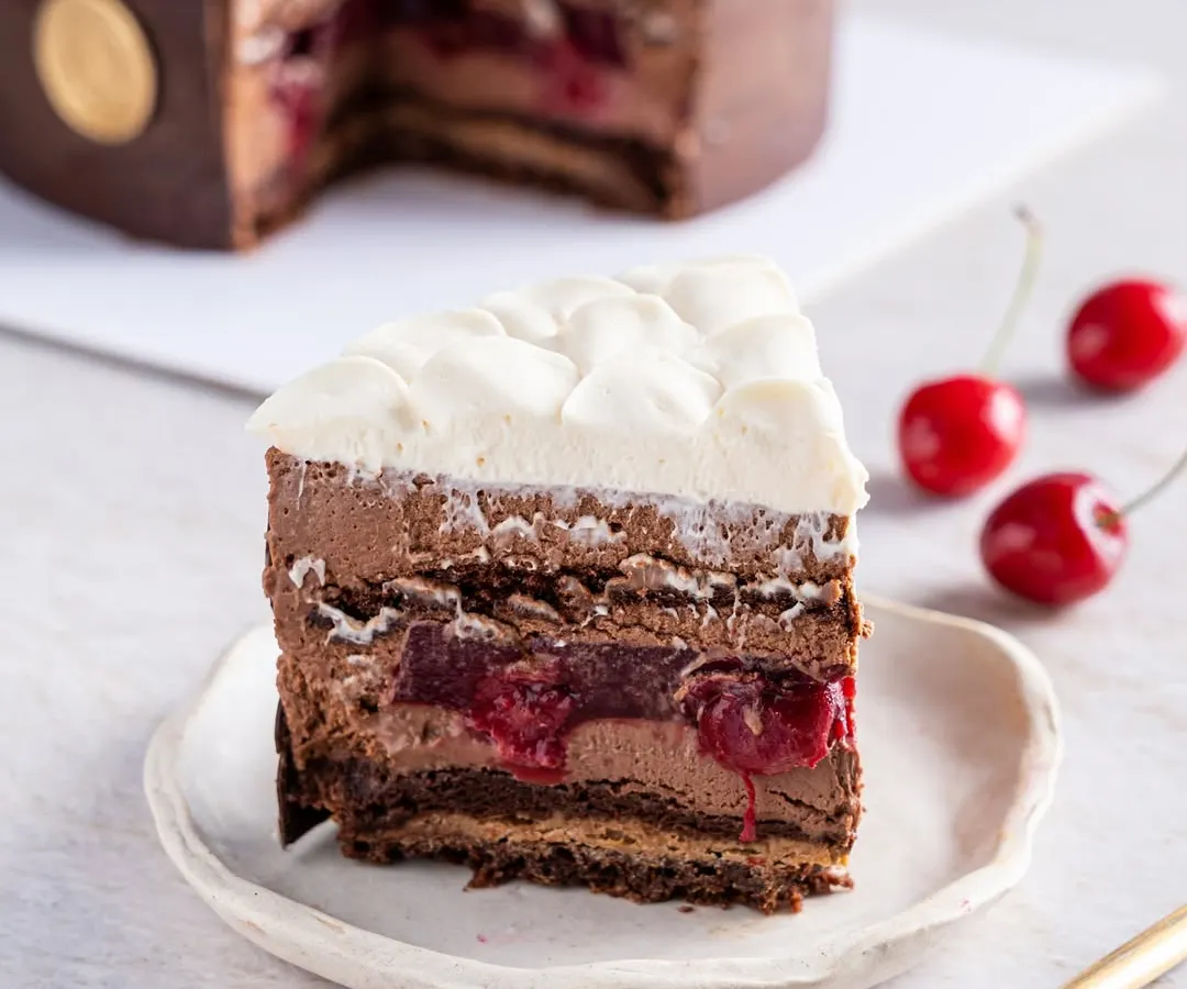 A perfect slice of our modern Black Forest Entremet, revealing layers of rich chocolate mousse, tangy cherry confit, and light whipped cream. This is a sophisticated reinterpretation of a classic, showcasing our dedication to flavour and texture.