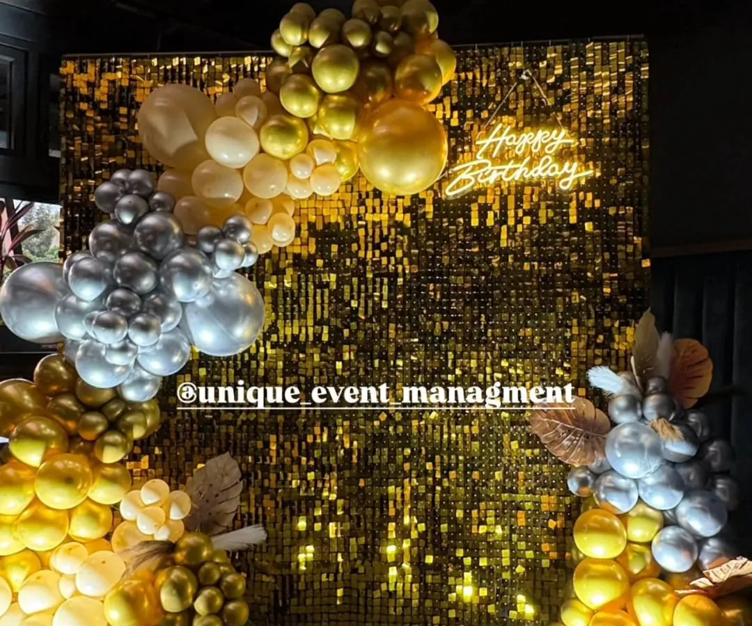 A glamorous 25th birthday party setup featuring a shimmering gold sequin wall that makes a perfect photo booth. We completed the look with a custom 'Happy Birthday' neon sign and organic balloon garlands in gold, silver, and white for a chic celebration.