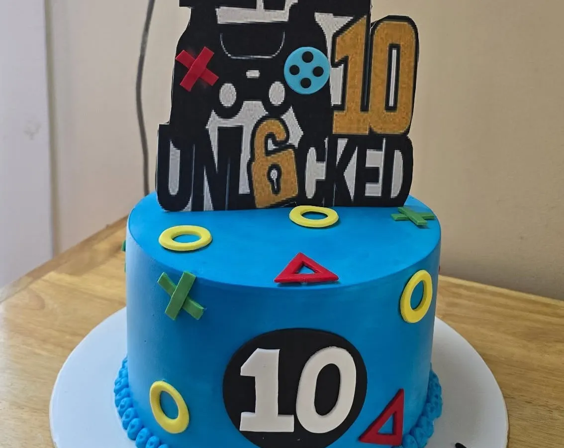 A blue gaming cake marks a tenth birthday, with a controller-themed topper and colourful game-button details around our cake.