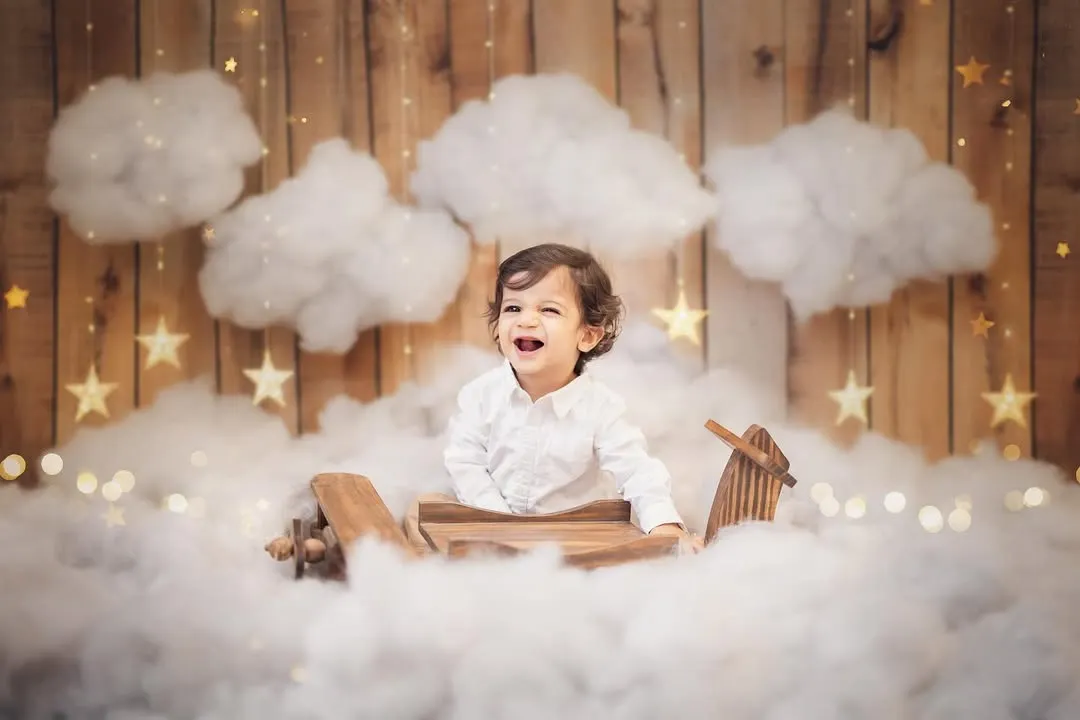 Pure, unfiltered joy. This little pilot's laughter is everything. For his first birthday photoshoot, we created a magical sky with a wooden airplane and fluffy clouds, making his milestone celebration truly unforgettable.
