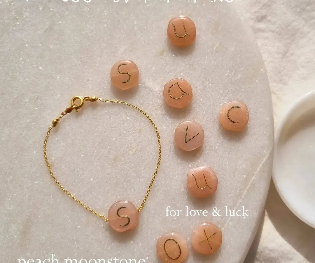Carry your strength on your wrist. My initial bracelets feature the same hand-embossed Peach Moonstone on a minimalist chain. Here you can see a selection of initials, each waiting to become part of your journey.