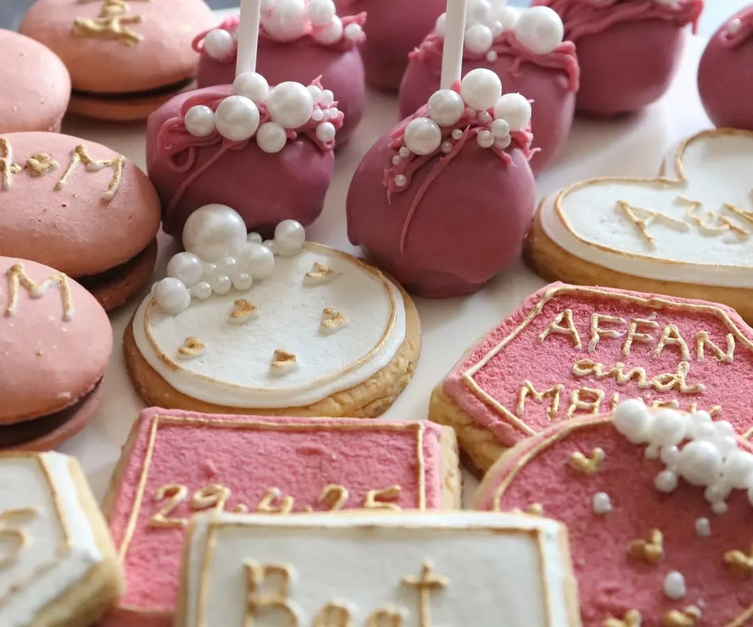 It's all in the details. 🫶🏻 Look at this close-up of the custom treats, including hand-piped cookies with the couple's names and date, pretty pink cake pops, and initialed macarons.