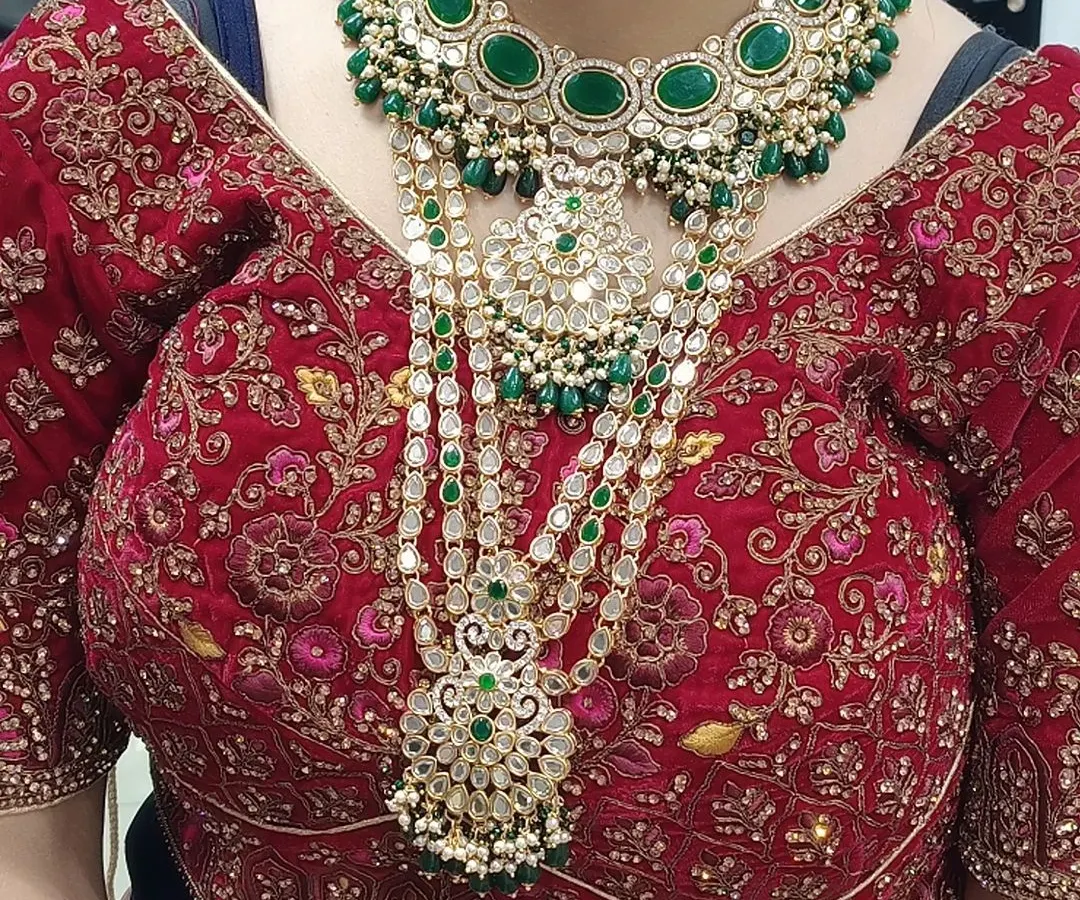 This is how a complete bridal set looks when worn. You can see the beautiful layering of the heavy choker and the long multi-layered haar, both featuring intricate work with green stones and kundan. This is the royal look every bride dreams of.