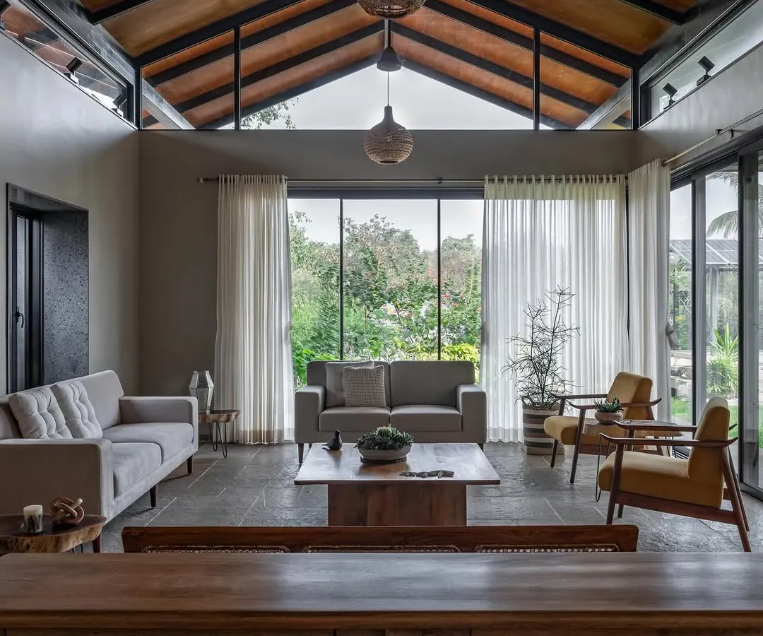 The living area of Grove House in Alibaug, designed as a gathering space for a veteran sailor and his family. The high, pitched roof and floor-to-ceiling glass walls dissolve the boundary between the interior and the surrounding coconut grove, creating a sanctuary filled with tropical light.