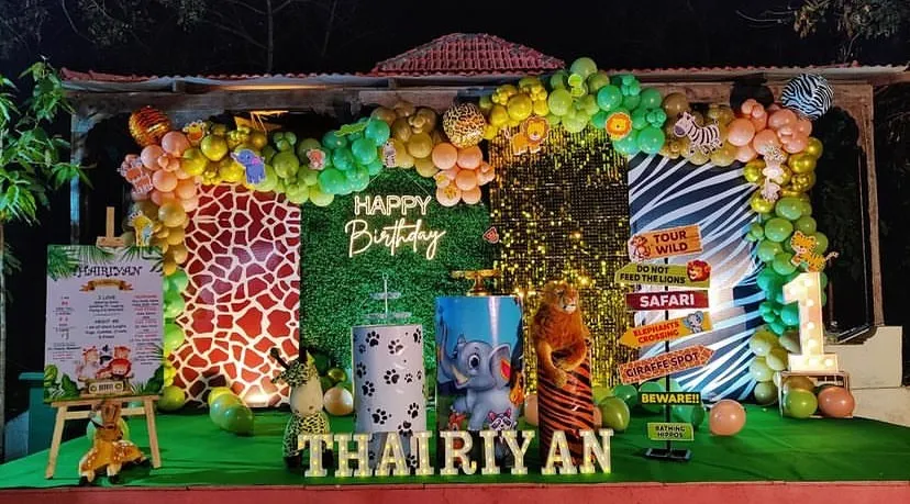 I bring the jungle to your party with this exciting safari-themed birthday decoration. The setup includes a lush green backdrop, animal print panels, an organic balloon arch in jungle colors, and fun props like animal figures and road signs to create an immersive adventure for a first birthday.