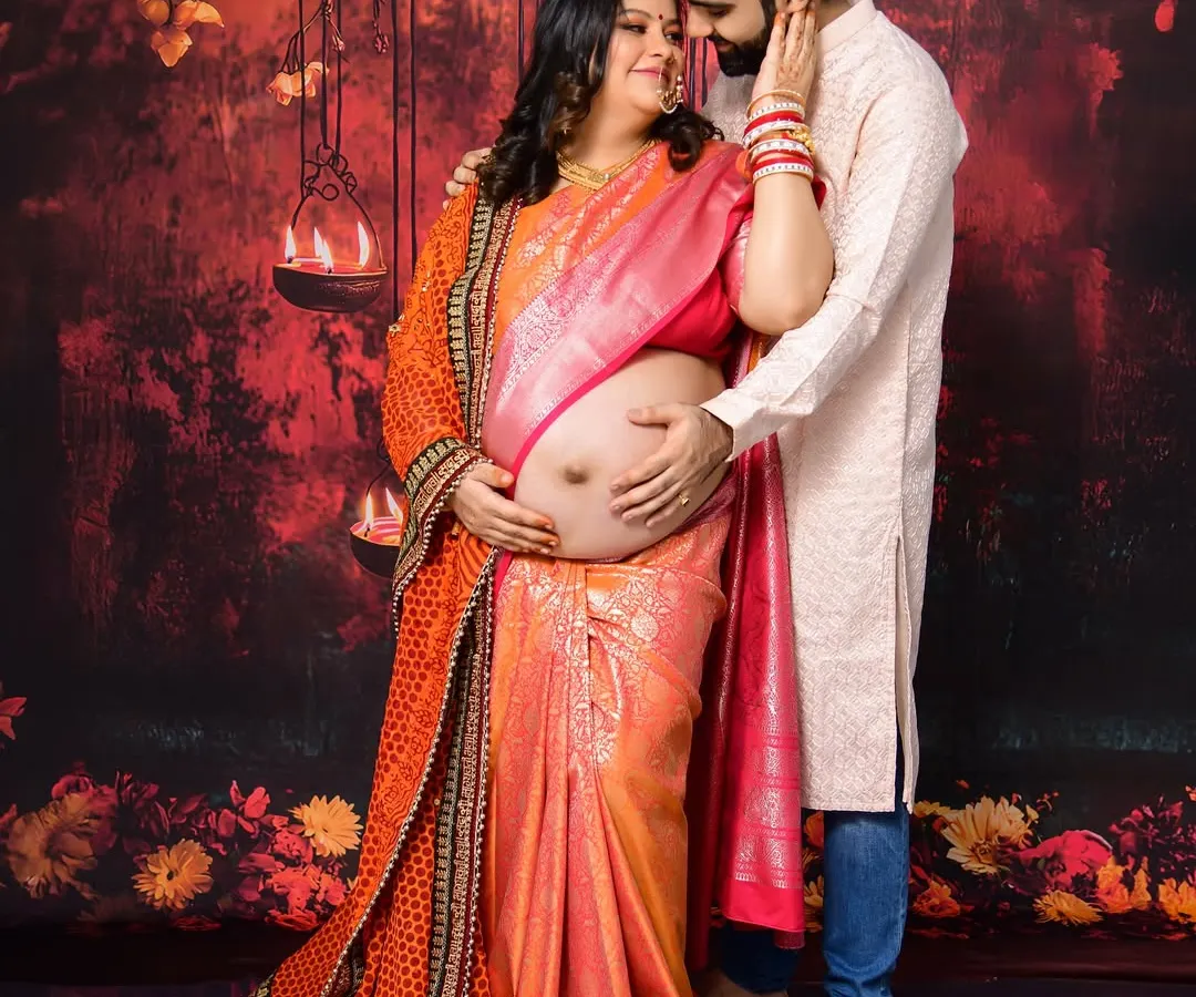 We love capturing the beauty of tradition. This couple's maternity portrait, set against a rich, warm backdrop with hanging lamps, highlights their connection and the elegance of a traditional saree, complete with intricate jewelry and henna.