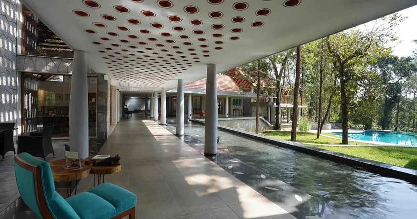 In this hospitality project, a long, open corridor runs alongside a tranquil water channel. The design, featuring a perforated ceiling and natural materials, creates a sensory journey that connects visitors to the surrounding coffee estate.