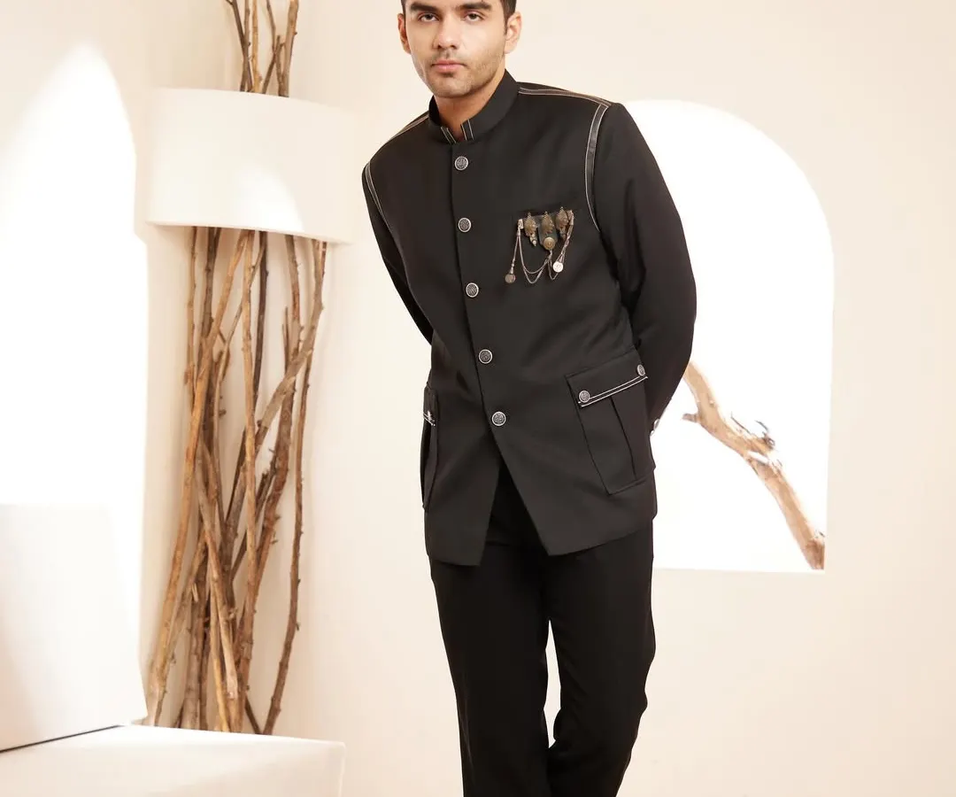 A modern interpretation of a timeless classic. This black bandhgala jacket features subtle leather piping and a distinctive metallic brooch, offering a sleek and sophisticated look for formal dinners and exclusive cocktail events.